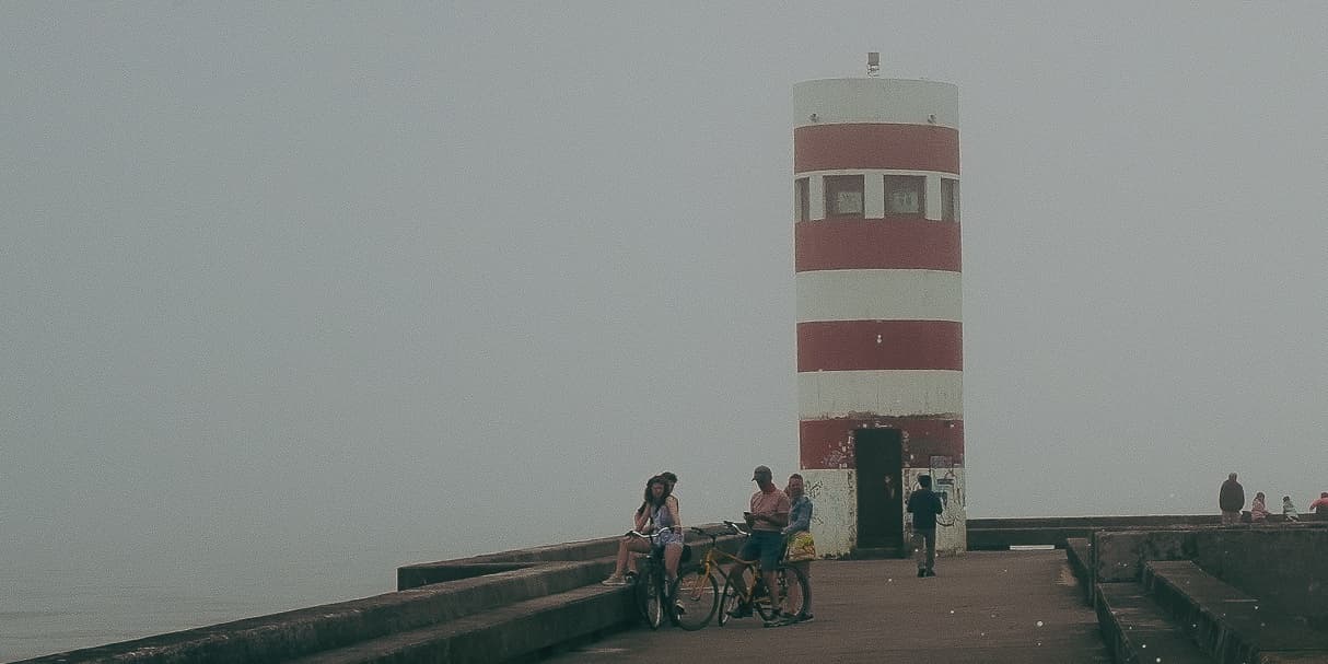 Visitors beside a striped lighthouse in coastal fog photographed by Eugene Truuts