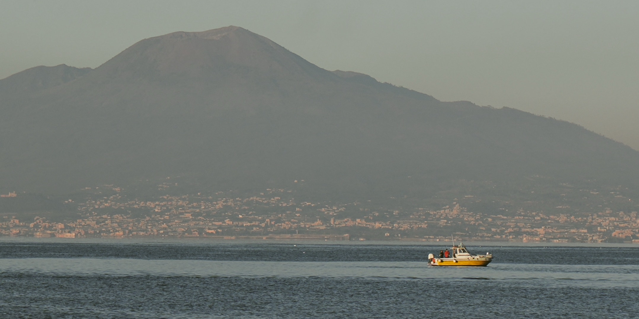 Yellow passenger boat crossing a bay beneath a volcanic mountain photographed by Eugene Truuts